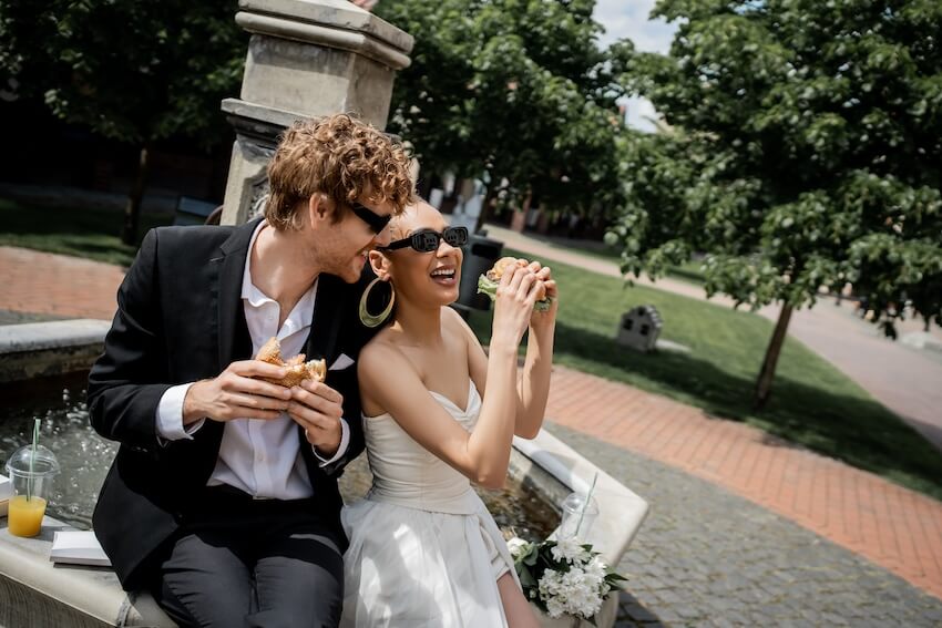 Wedding ceremony ideas: bride and groom happily eating burgers outdoors